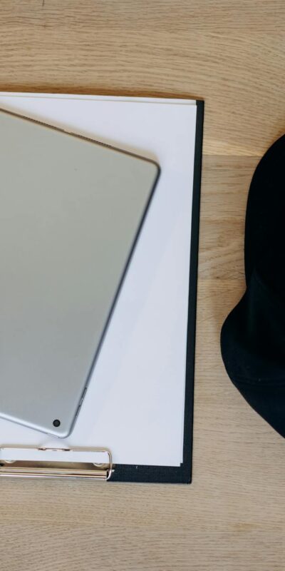 A stylish flat lay of a clipboard, tablet, and cap on a wooden desk, perfect for productivity themes.